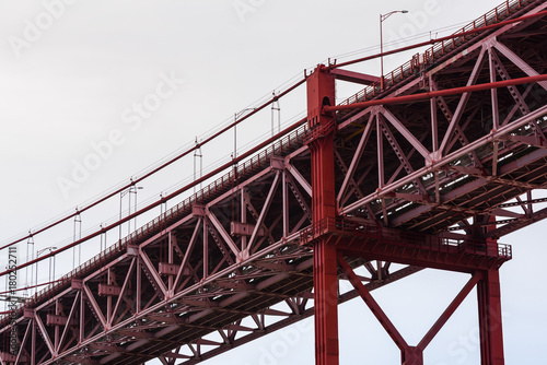 Close-up of red steel beam suspension bridge against grey sky © Magnus