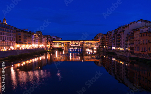 Ponte Vecchio bridge in Florence at night time with city lights reflecting in Arno river.