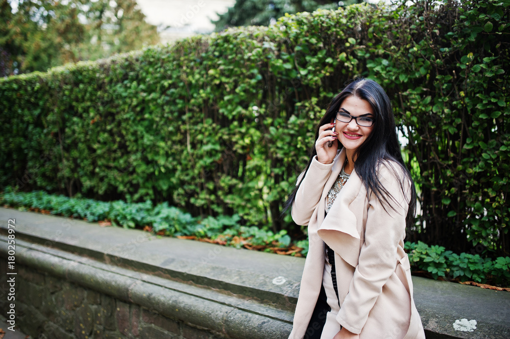 Black hair sexy woman in glasses and coat posed on street with mobile phone. Black hair sexy woman in glasses and coat posed on street with mobile phone.