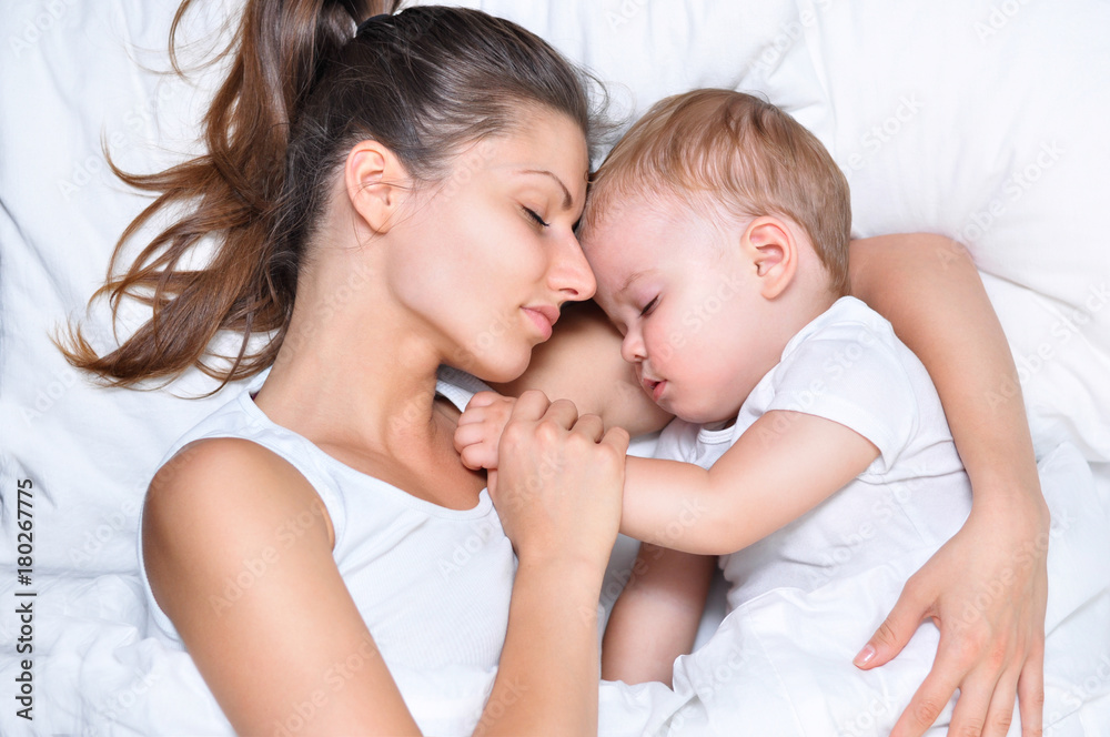 young beautiful mother hugs with her sleeping little cute son on white linen young beautiful mother hugs with her sleeping little cute son on white linen