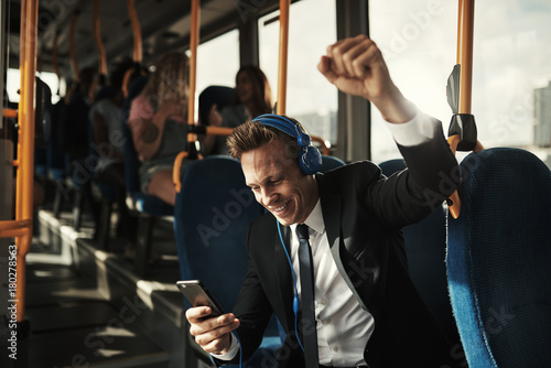 Young businessman reading texts and celebrating during his morning commute