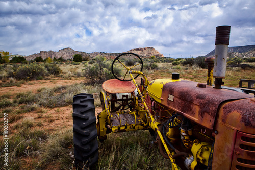 A textured and colorful old tractor sits in the New Mexico desert, with mesas and cloud-filled sky in the background