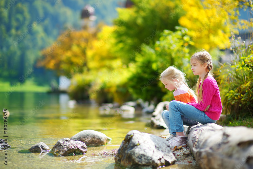 Adorable sisters playing by Hallstatter See lake in Austria on warm summer day. Cute children having fun splashing water and throwing stones into the lake. Adorable sisters playing by Hallstatter See lake in Austria on warm summer day. Cute children having fun splashing water and throwing stones into the lake.