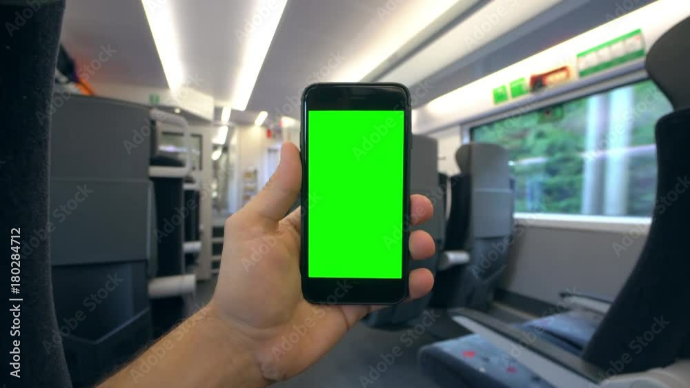 A hand holding (using) a smapthone with a green screen on the train. Close-up shot A hand holding (using) a smapthone with a green screen on the train. Close-up shot
