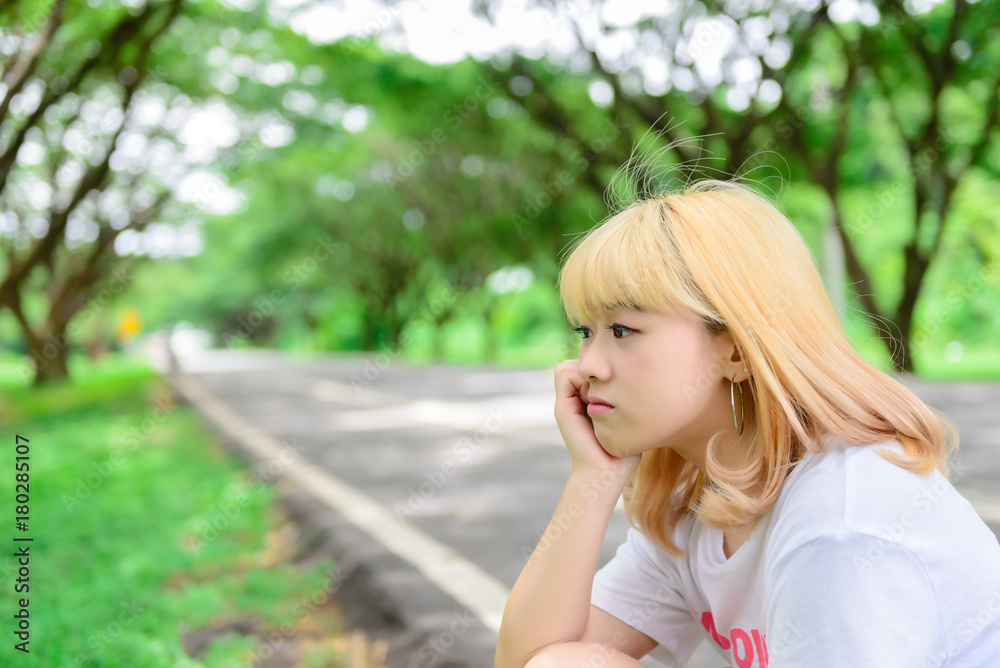 Obraz premium Portrait of asian young girl sit at tunnel trees,Beautiful thai woman take a photo outdoors,sad woman concept,she think over from love,heartbroken from boyfriend