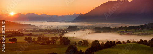 Breathtaking morning lansdcape of small bavarian village covered in fog. Scenic view of Bavarian Alps at sunrise with majestic mountains in the background.