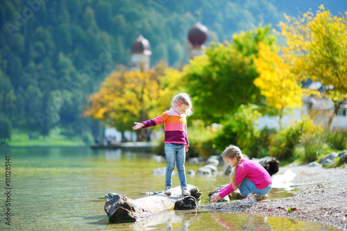 Adorable sisters playing by Hallstatter See lake in Austria on warm summer day. Cute children having fun splashing water and throwing stones into the lake.
