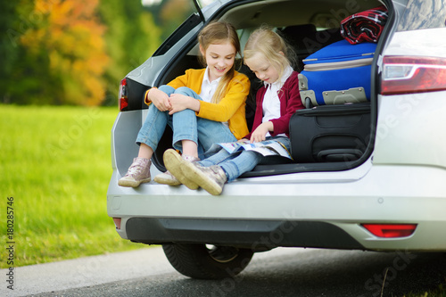 Two adorable little girls ready to go on vacations with their parents. Kids sitting in a car examining a map. © MNStudio