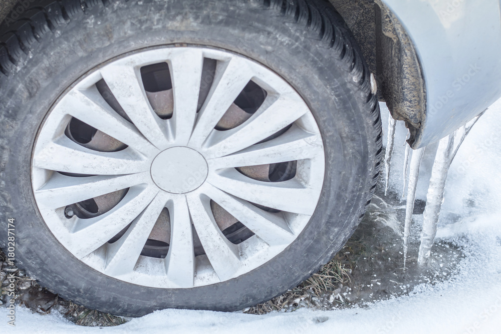 Huge icicles on the dirty car wheel. Dangerous Frozen ice build up wheel fender arch. Driving problems. Extreme winter snow series. Close up tire on the snowy road.