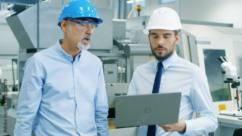 Head of the Department Holds Laptop and Discusses Product Details with Chief Engineer. They Wear Hard Hats and Work in the Modern Factory. Medium Shot. Shot on RED EPIC-W 8K Helium Cinema Camera. Head of the Department Holds Laptop and Discusses Product Details with Chief Engineer. They Wear Hard Hats and Work in the Modern Factory. Medium Shot. Shot on RED EPIC-W 8K Helium Cinema Camera.