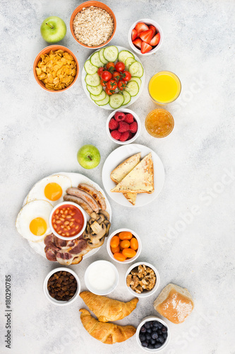 Filling breakfast with eggs sunny side up  sausages  bacon and mushrooms with fruits and vegetables  breads and juice on the grey white table  top view  copy space  vertical  selective focus