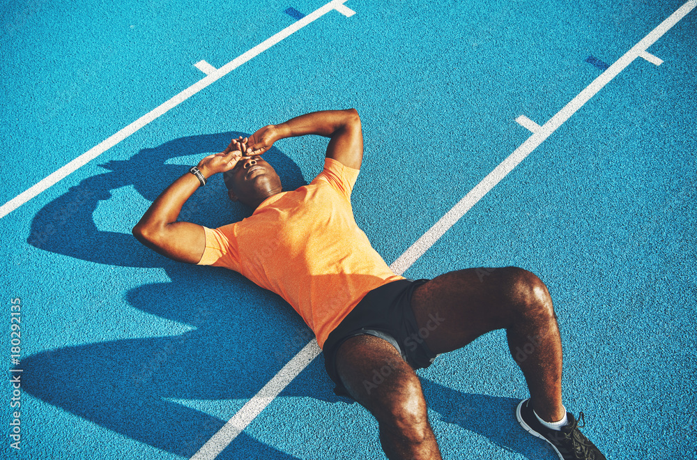 Fototapeta Exhausted young athletic lying on a running track after training