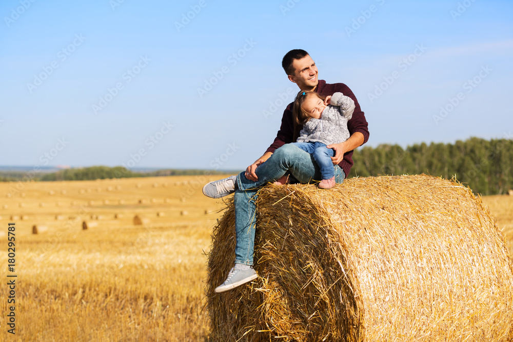 Happy father and 2 year old girl sitting on hay bales in harvested field Happy father and 2 year old girl sitting on hay bales in harvested field
