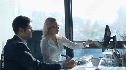 Two business professionals, man and woman, working together in office, looking at data on computer / Business professionals working together