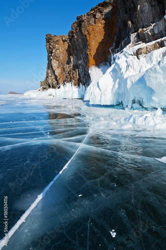 Lake Baikal in the winter. Blue smooth ice and icy coastal rocks of Olkhon Island in a sunny frosty day