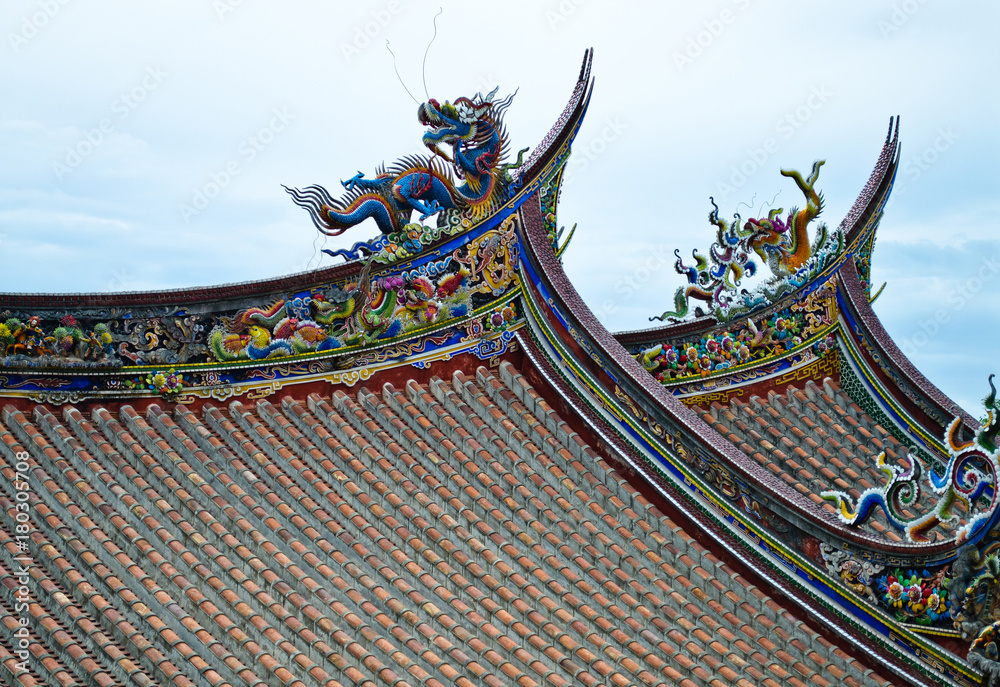 Fototapeta premium Chinese temple roofs. One blue and one yellow dragon on each roof. Phoenix and other historical characters along the edge of the roof all painted in red, yellow, blue, green and white colors.