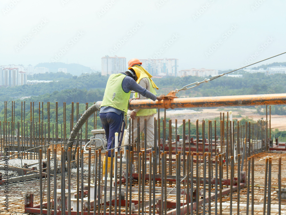 Construction workers pouring wet concrete using concrete hose from