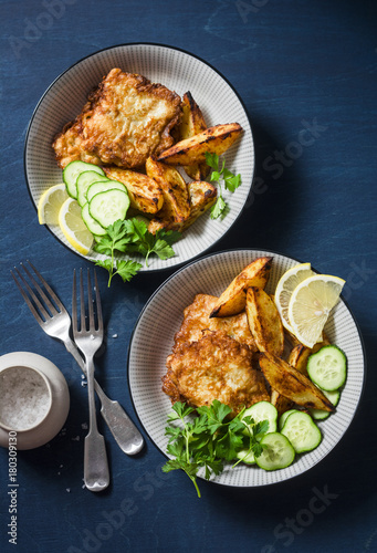 Two bowls with deep-fried fish and garlic baked potatoes on a blue background, top view. Fish and chips. Flat lay