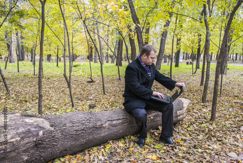 Businessman having a laptop in the park in the fall. A man is working at a computer in the park. Businessman having a laptop in the park in the fall. A man is working at a computer in the park.