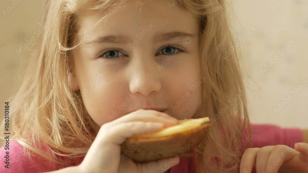 A little girl is eating a sandwich with cheese. The child eats bread and cheese. A little girl is eating a sandwich with cheese. The child eats bread and cheese.