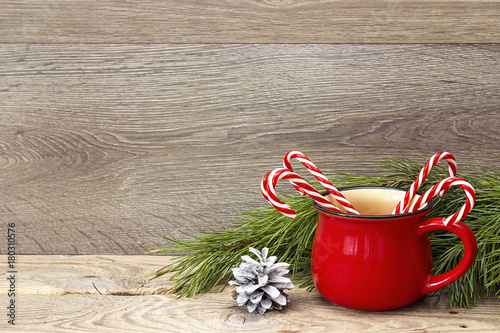 Red cup with striped Christmas candy canes against wooden background. Copy space.