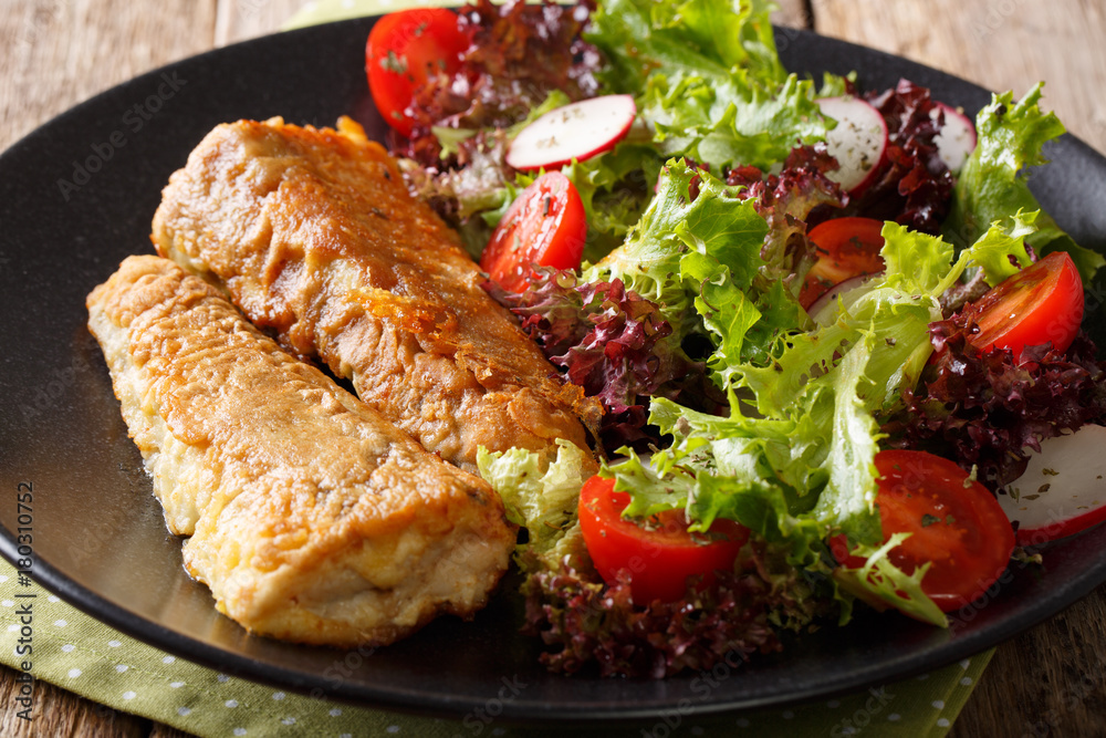 Healthy lunch: fried hake with tomato, radish and lettuce salad close-up. horizontal Healthy lunch: fried hake with tomato, radish and lettuce salad close-up. horizontal