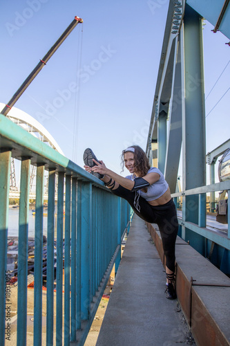 Beautiful young girl stretching with leg up at the bridge. She is warming before jogging