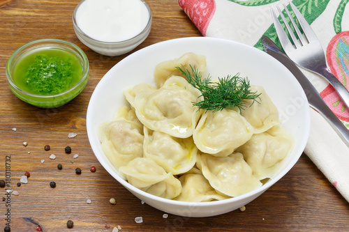 Meat dumplings - russian pelmeni, ravioli with meat on a white plate on a wooden background
