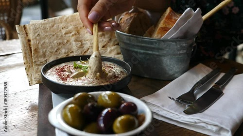 Closeup Hand Dips Bread Stick In Healthy Hummus With Olives And Fresh Pita Bread photo