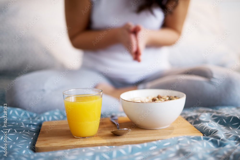 Close up of breakfast and juice on a wood saucer on the bed while the woman behind sitting and prying. Close up of breakfast and juice on a wood saucer on the bed while the woman behind sitting and prying.