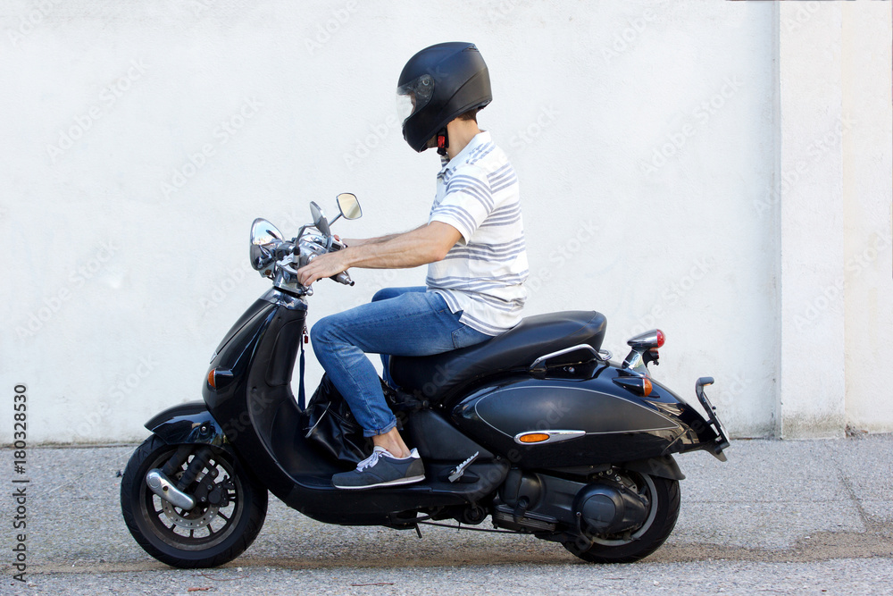 Obraz premium Widok z boku młodego człowieka w kasku, jazda na skuterze na drodze