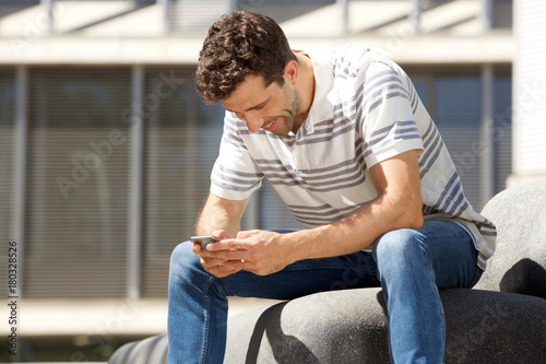Young guy sitting outdoors and sending text message on mobile phone