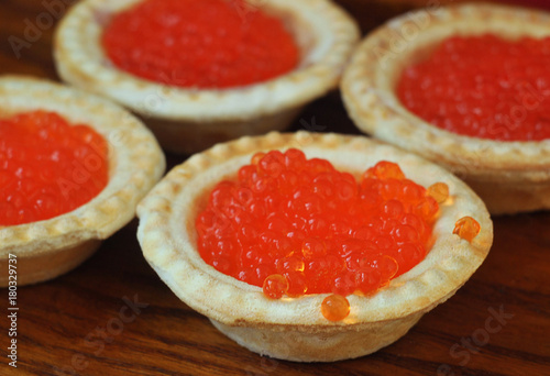 Tartlets with red caviar on a wooden plate.