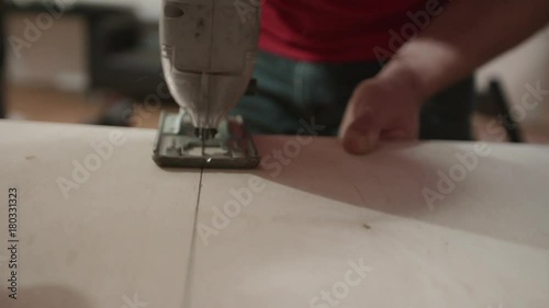 Closeup slow motion shot of carpenter sawing wooden planks. Cutting panel with jigsaw. Handyman using automatic electric handy saw on the woodwork workshop table. Manual work concept. photo