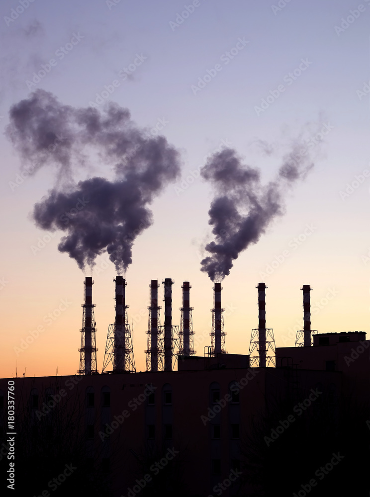Industrial landscape with black silhouette of electric power station with many high smoke pipes in the evening after sunset over cloudless red and violet sky