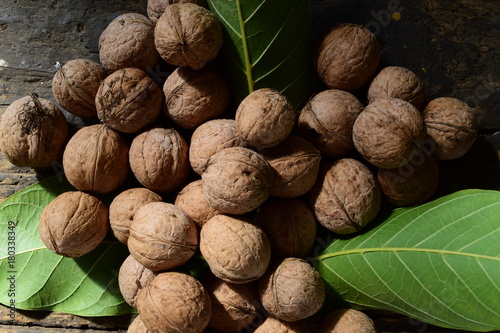 a pile of walnuts and green leaves of walnut on a dark wooden table