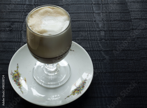 a beautifull glass with coffee latte with high foam of cream and saucer on the black background photo