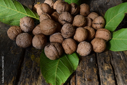 a pile of walnuts and green leaves of walnut on a dark wooden table