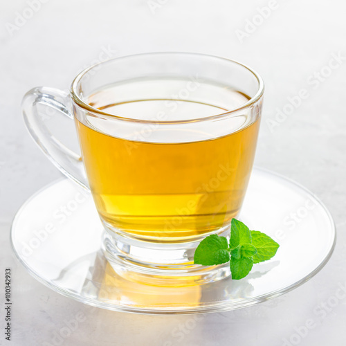 Herbal mint tea in a glass cup with fresh peppermint on background, square format