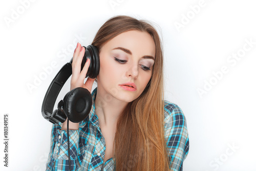 Headshot of a young adorable blonde woman in blue plaid shirt enjoying listening music to big professional dj headphones. photo