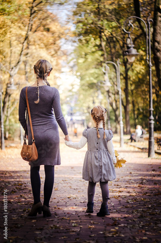 Mother with daughter walking in the park in autumn holding hands.