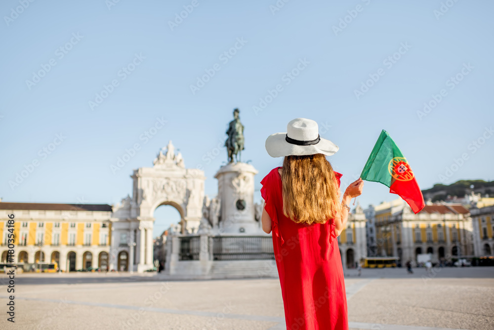Lifestyle portrait of a young woman tourist with portuguese flag standing on the main square during the morning light in Lisbon city, Portugal