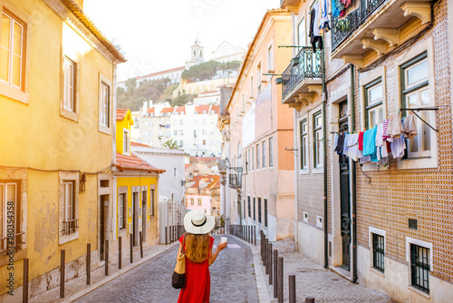 Woman tourist walking back on the narrow street in Alfama region during the morning light in Lisbon, Portugal