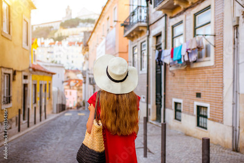 Woman tourist walking back on the narrow street in Alfama region during the morning light in Lisbon, Portugal