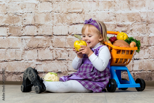 The child, a little girl with a cart full of vegetables and fruits. Purchase of products in the supermarket.