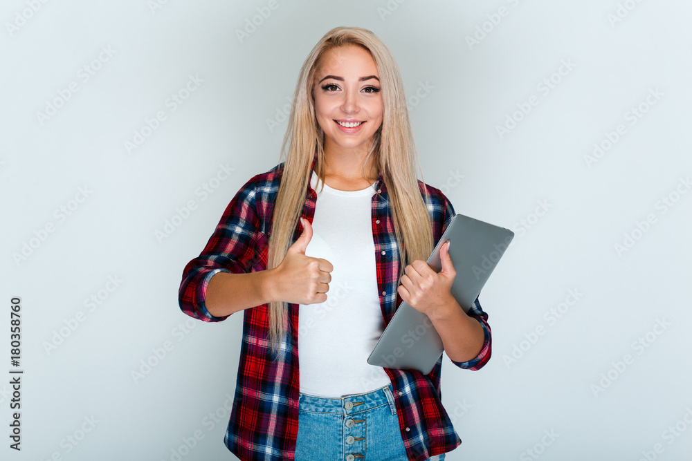 That is success! Beautiful young woman with blond hair holding her laptop and looking at camera with smile while standing against grey background That is success! Beautiful young woman with blond hair holding her laptop and looking at camera with smile while standing against grey background