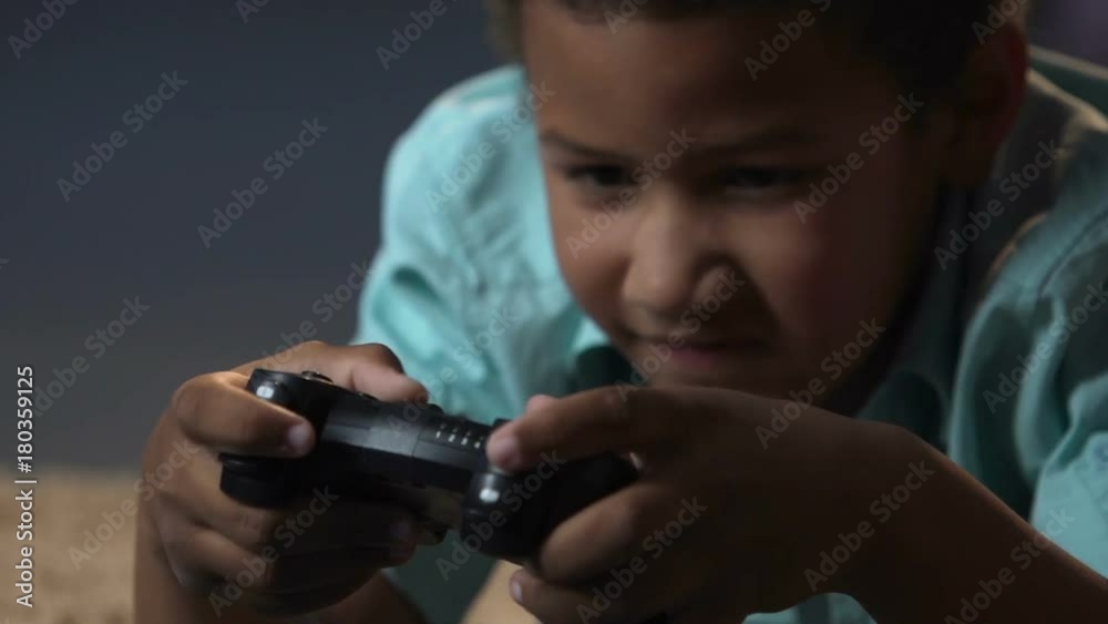 Mixed-race boy lying on floor with play station control and playing video games Mixed-race boy lying on floor with play station control and playing video games