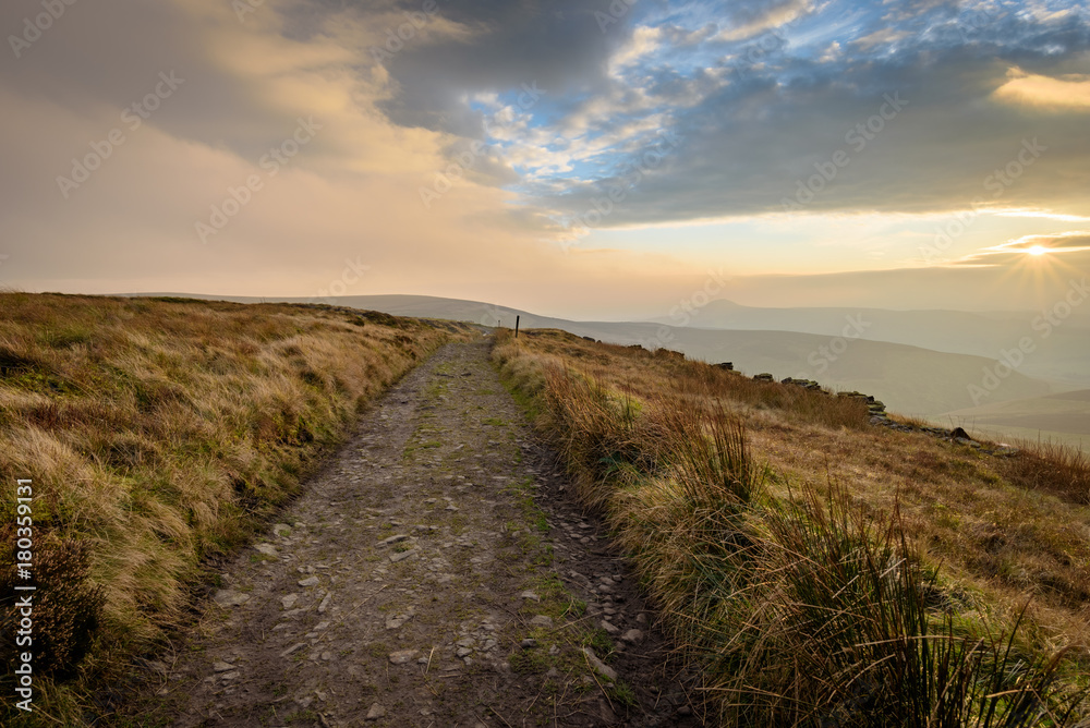 Beautiful autumn scenery in the Peak District - layers of hills and sunlight with dramatic clouds hanging over the mud track