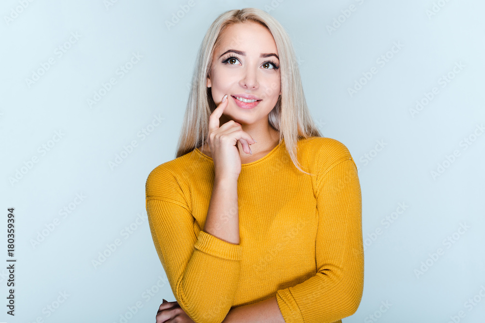 Maybe I should try something new! Beautiful young woman with blond hair keeping hand on chin while standing against grey background Maybe I should try something new! Beautiful young woman with blond hair keeping hand on chin while standing against grey background