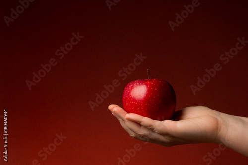 A Hand giving an apple isolated on a christmas red background. Compassion and generosity concept.